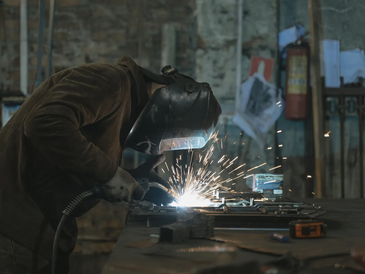 Worker welding metal components inside an industrial fabrication workshop